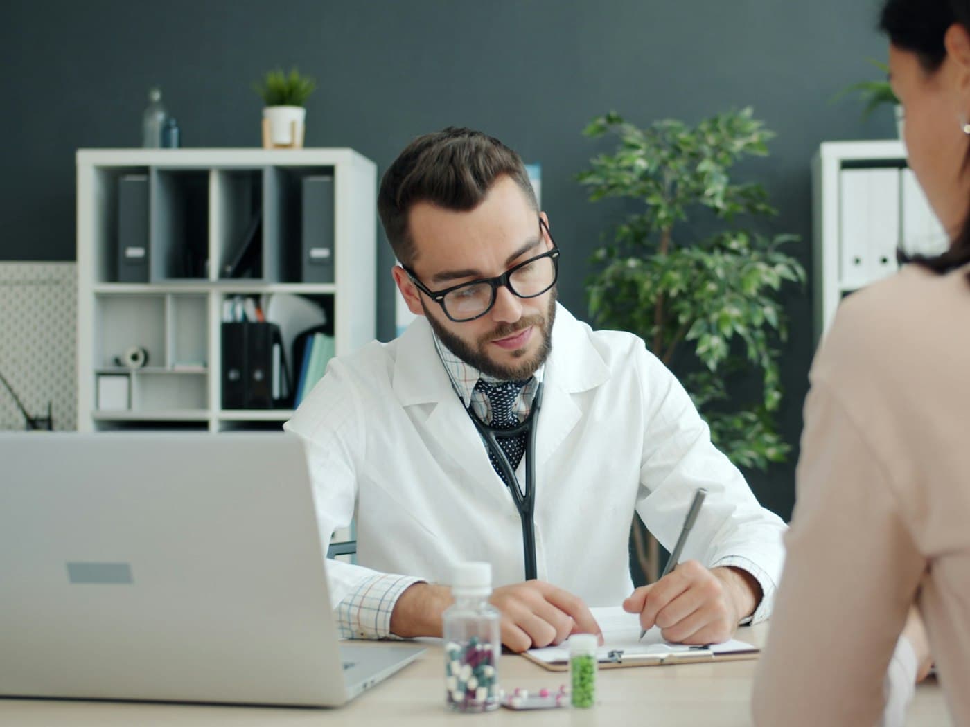 Médecin consultant le dossier d’un patient sur son ordinateur portable, en présence du patient